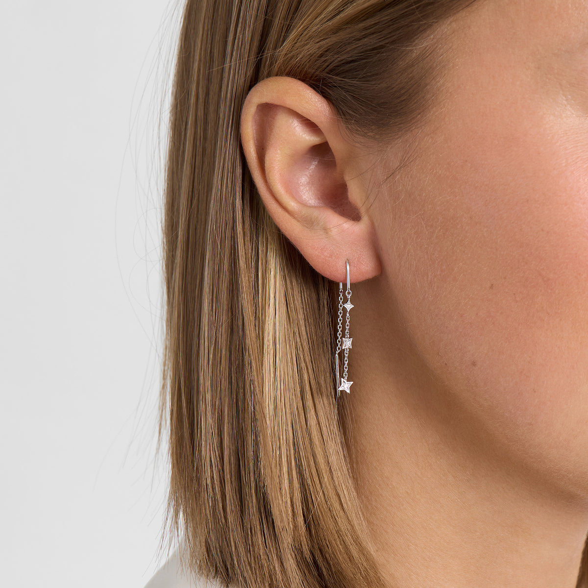 Silver earring with star pendant shown on ear, model's left side profile