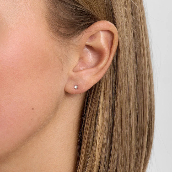 Discreet ear stud in silver with clear stone, shown on the ear from the front. Simple and elegant style.