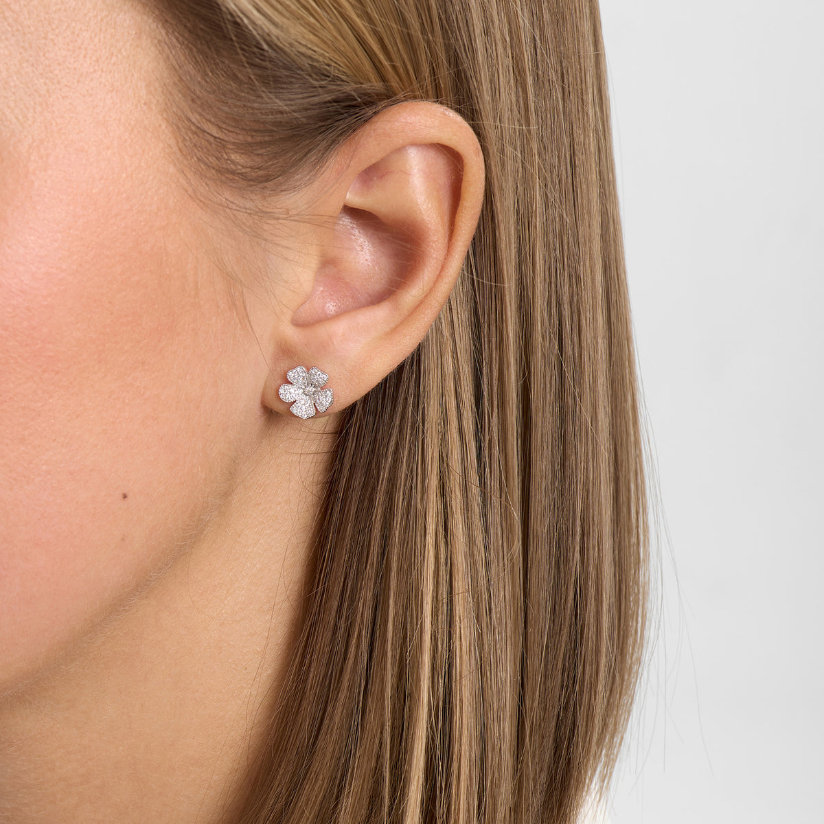 Floral earrings in silver with small stones, worn on the ear, front view of the piece of jewellery