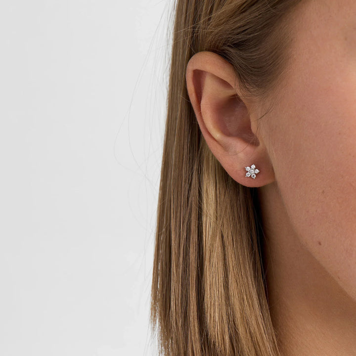 Earrings in silver with floral motifs and clear stones, shown on ear in profile picture