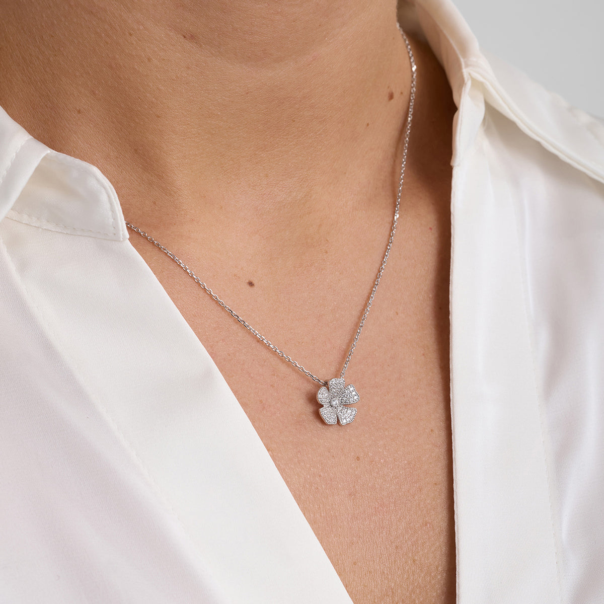 Necklace with silver four-leaf clover pendant, worn by woman wearing white shirt, front view