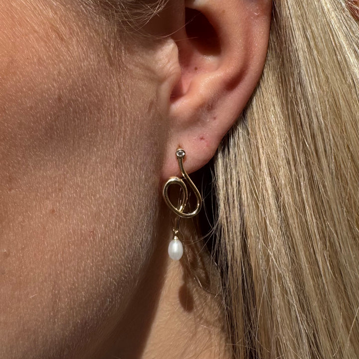 Guld ørering med perle og lille diamant, vist på en model. Elegant design i guld med hvid perle.