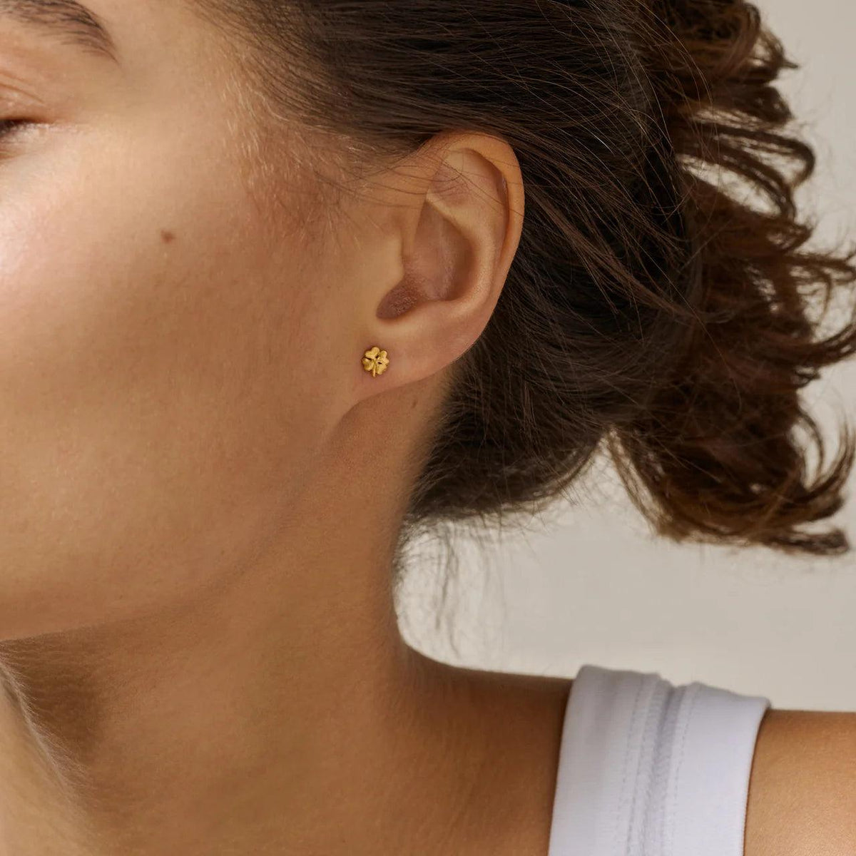 Enamel Organic Clover small four-leaf clover studs in gilt appear worn on the ear, Model E412GM-1.