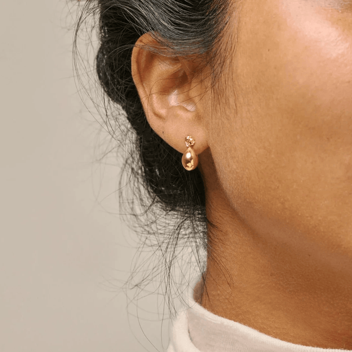 Enamel Poe Studs gold plated earrings are worn in the ear, showing elegant drop shaped golden detail. Model e385gm