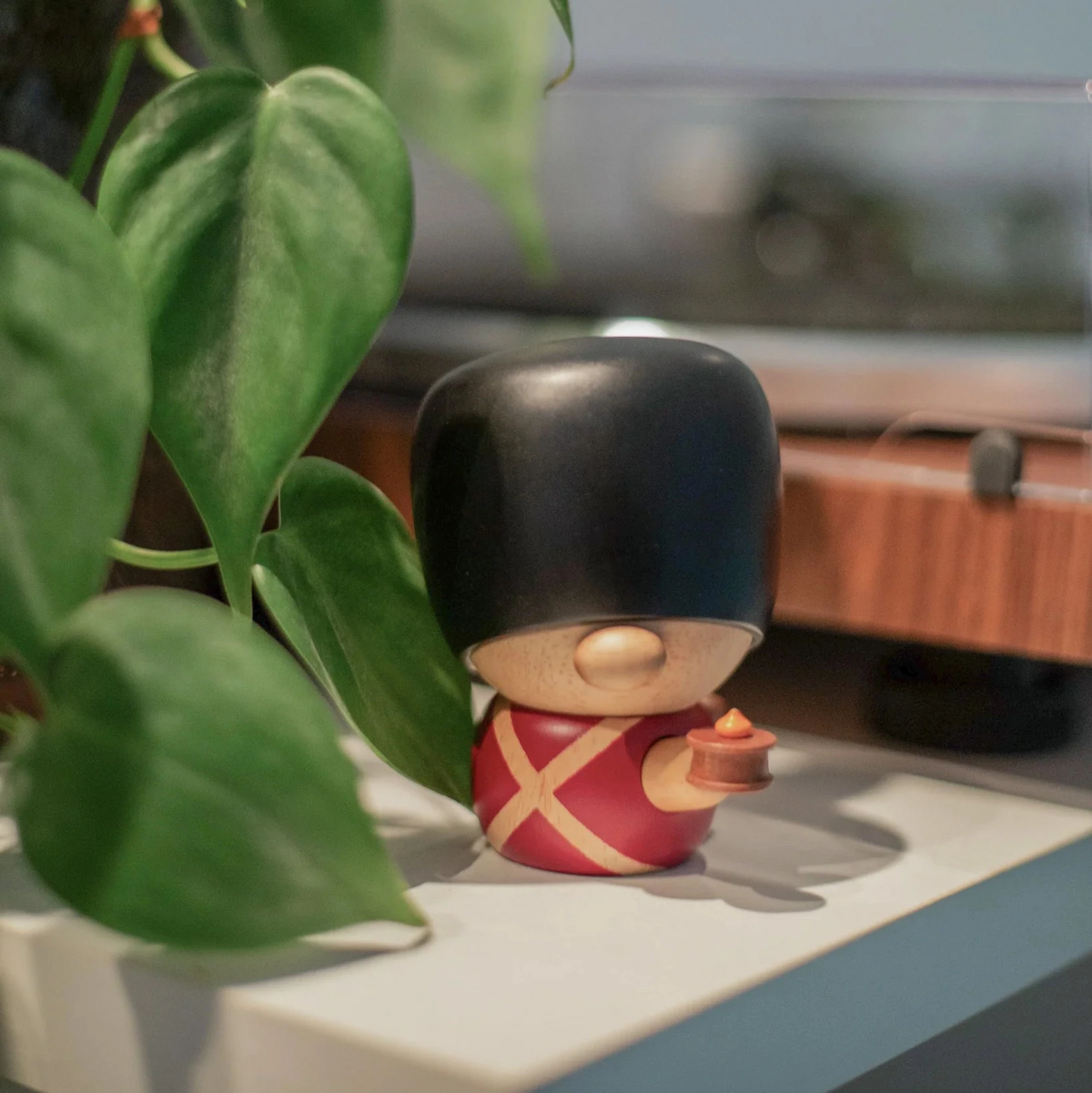 Fablewood HC Andersen's Fyrtøjet-8005-1 wooden figure of guards in red uniform and black bearskin hat on shelf by green plant. Model 8005-1