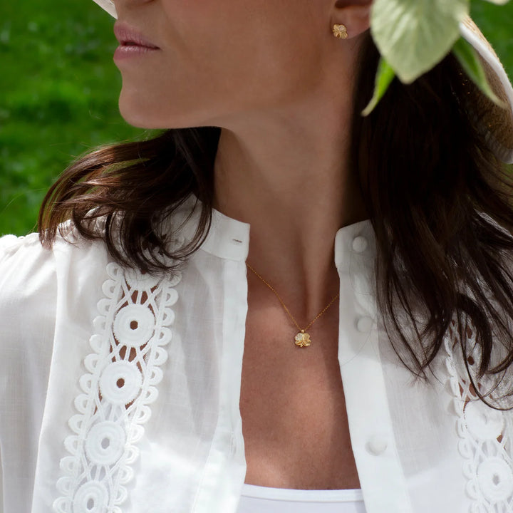 Flora Danica Firklover Necklace Pave Gilded worn outdoors, gold clover pendant on woman in white blouse. Model 907-FLC-NE-G-POPE.