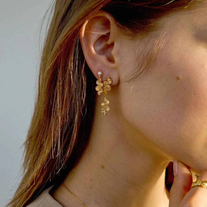 Hultquist Copenhagen Audrey Pearl gold-plated earrings with pearls and wavy details appear on the ear. Model S08586G-2.
