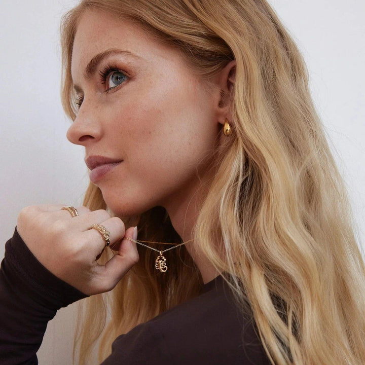 Jeberg I AM Zodiac necklace gold-plated zodiac worn by woman with wavy light hair. Model 42400-001.