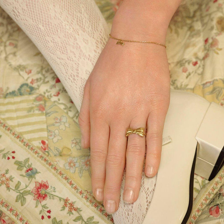 Maanesten Satin gold-plated ring Bow appears on hand with delicate lace and cream shoe, Model 4832a-002-1