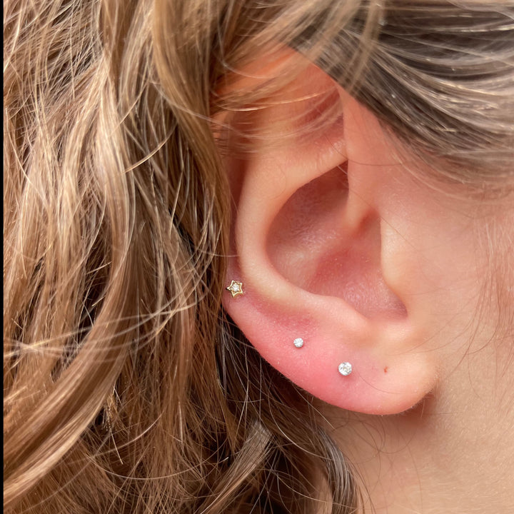 Maria Tash Diamond Solitaire Star white gold XSSTARD-WG-W3-001-2 is shown placed in the ear, star shaped with diamond detail. Model XSSTARD-WG-W3-001-2