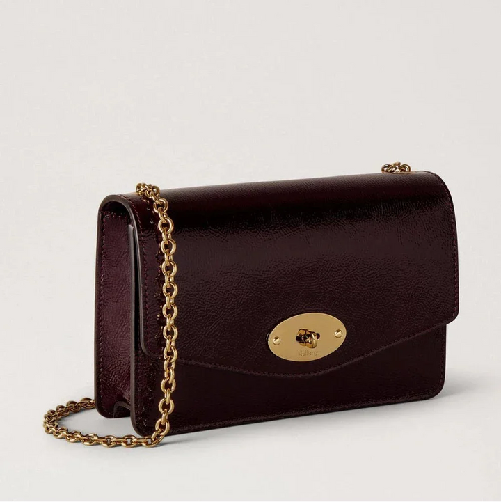 Mulberry Small Darley Deep Aubergine Patent shows a small, glossy shoulder bag in dark aubergine leather with a golden chain strap. Model RL8922737V697