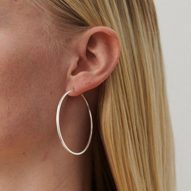 Pernille Corydon Orbit Store Hoops in silver are shown worn in the ear of a model with light hair. Model E-053-S