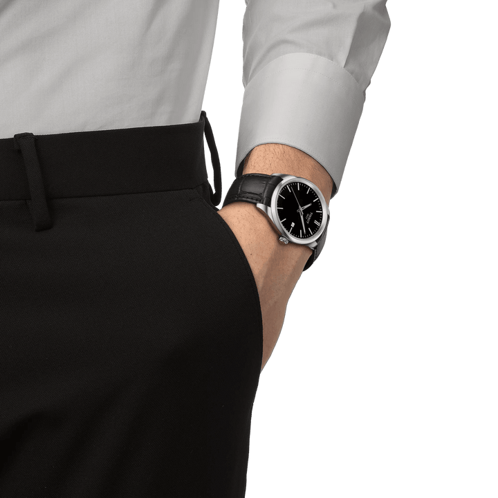 Tissot PR 100 Quartz with black dial and black leather strap is seen on a men's arm in formal wear. Model T1504101605100