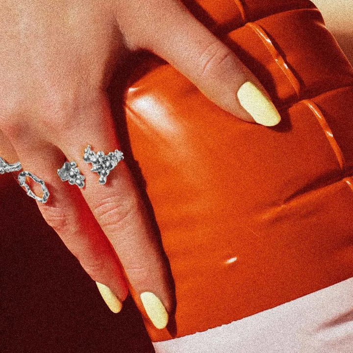 Vincent Orb Chronicles Solv Ring, elegant silver ring with organic design on hand with bright nails in front of orange background. Model VJ163-URS-001-2