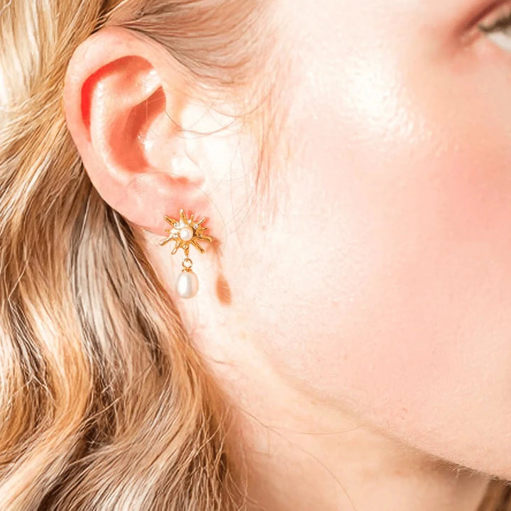 Vincent Rhea Gold Plated Pearl Earrings shown on ear, detail of sun shaped design with dangling pearl. Model VJ234-UEG-1