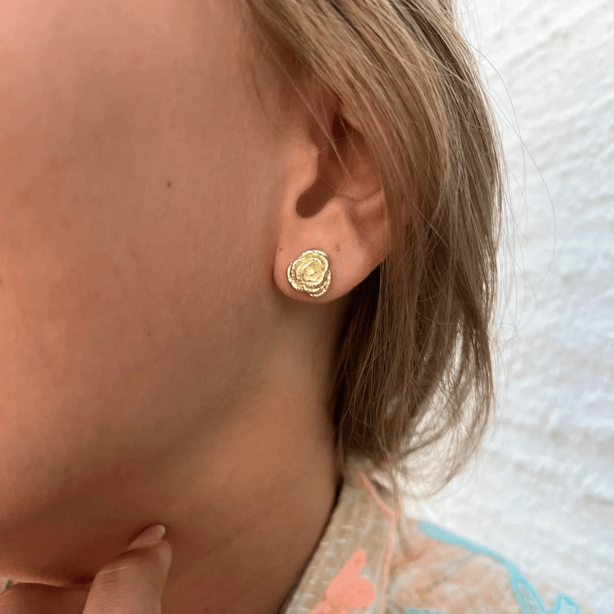 wioga-diana-gold-plated-rose ear studs worn on ear, gold-plated flower-shaped ear stud in close-up. Model E-8811-GP-1