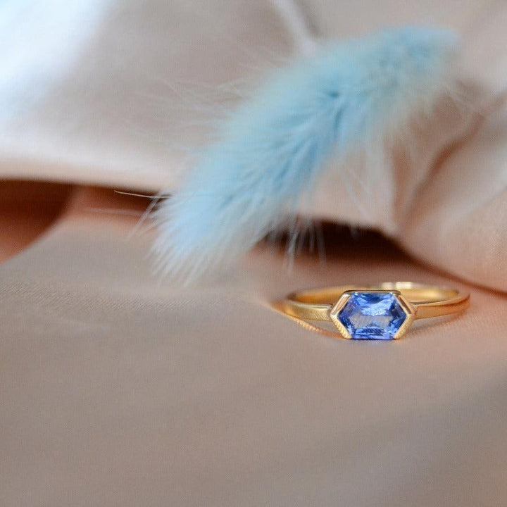 anpe-atelier-customized-ring-with-blue-sapphire shown on beige fabric, hexagonal blue sapphire in gold. Model27-blasafir-001-2
