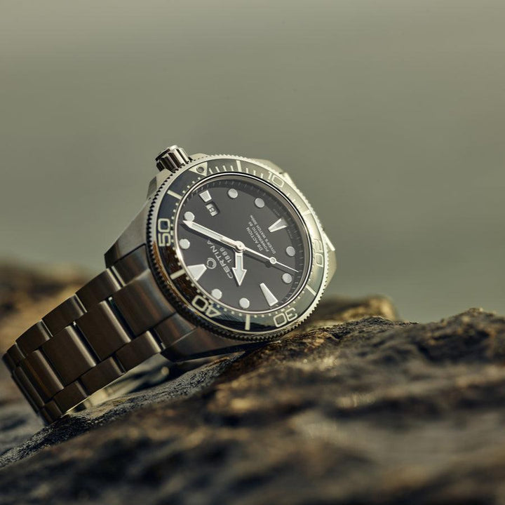 Certina DS Action Powermatic 80 men's watch with black dial and steel chain on rock. Model C0326071105100