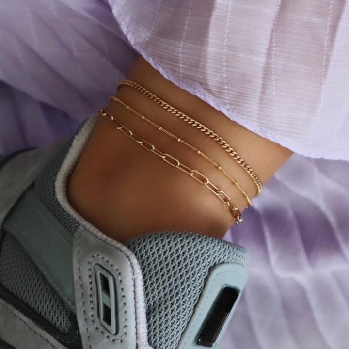 Jeberg Jewelery Saga Paner Anklet in gold-plated silver is displayed on the ankle along with other chains. Model 4535-G-4535-G-2