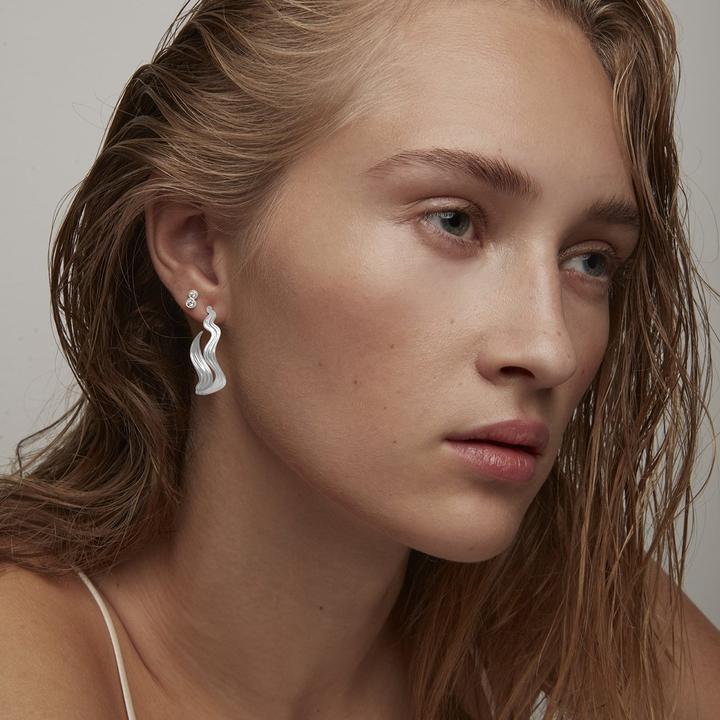 Polar Jewelry The World Hoop Solv is shown worn by model, silver colored wavy earring, Model hp-sl-00211-2